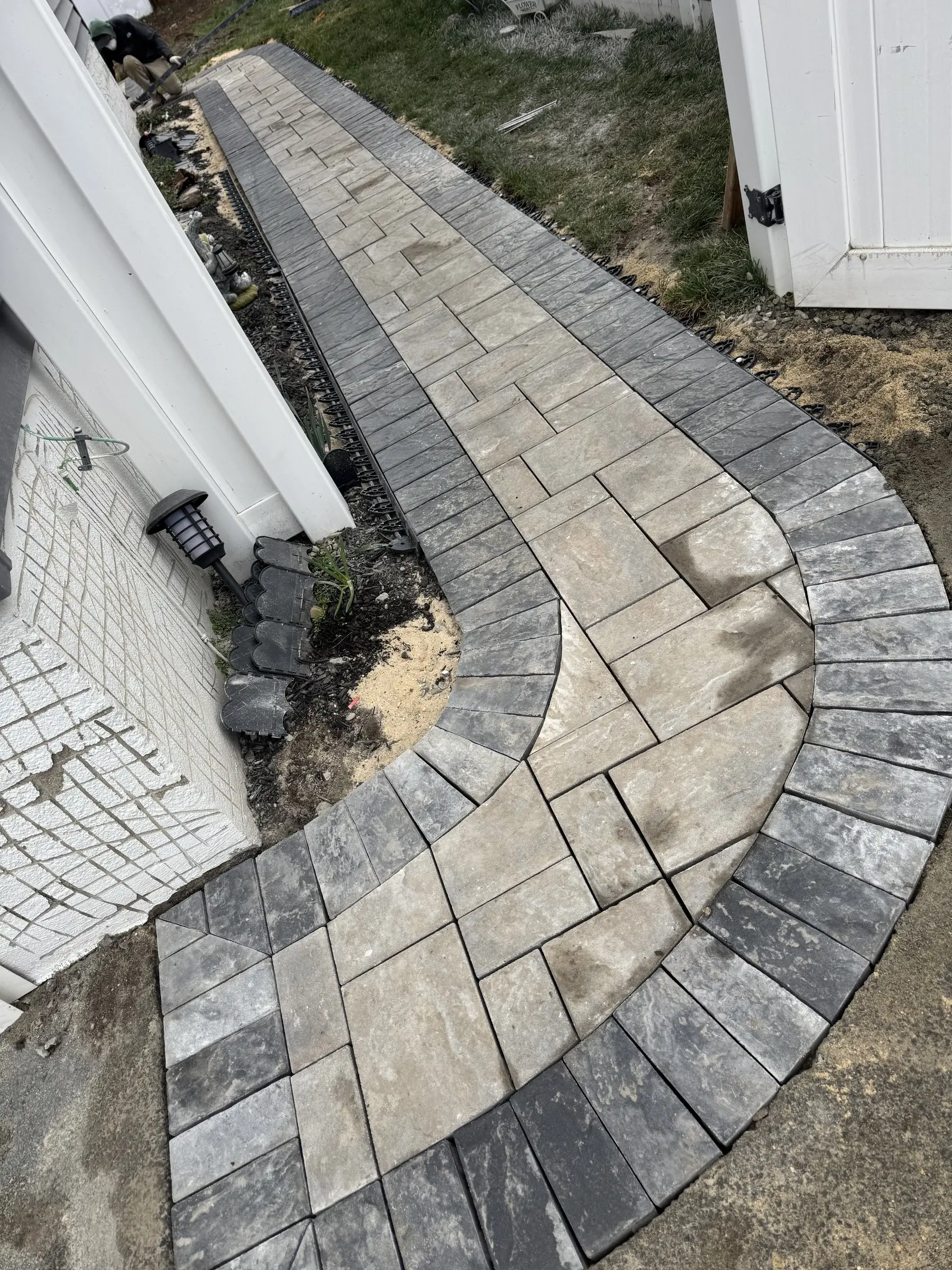 Curved paver walkway with a dark border along a house